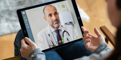 Personne tenant une tablette entre les mains et faisant une visioconférence avec un médecin